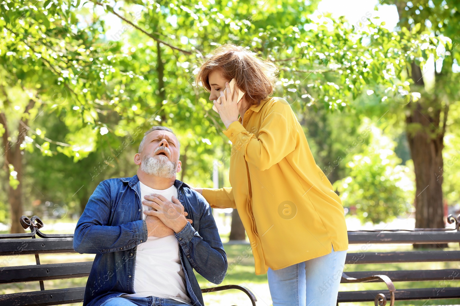 Photo of Woman calling ambulance for mature man having heart attack, outdoors