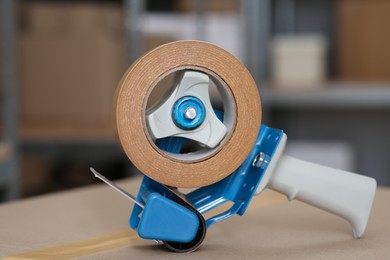 Photo of Adhesive tape dispenser on cardboard box indoors, closeup