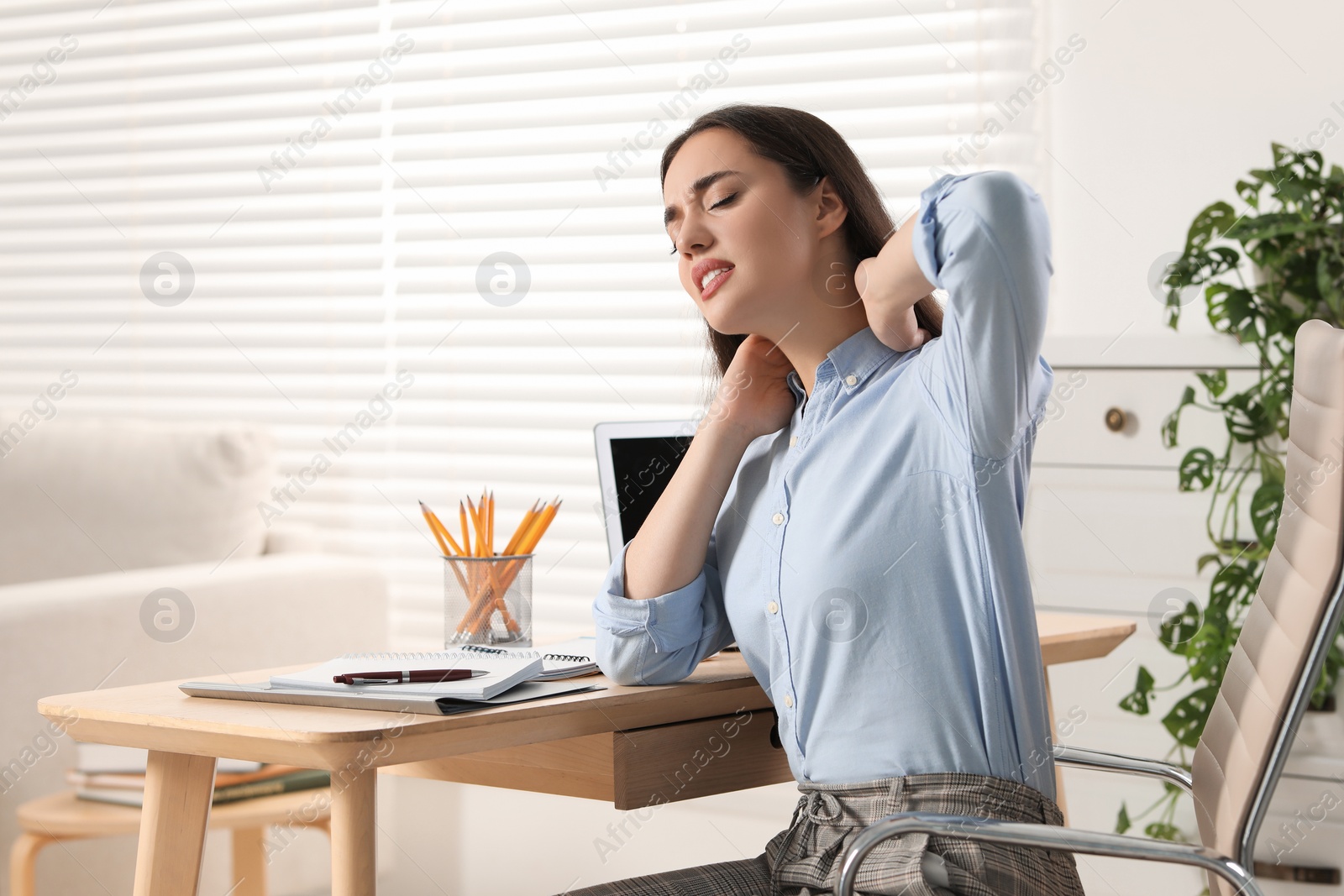 Photo of Young woman suffering from neck pain at table in office