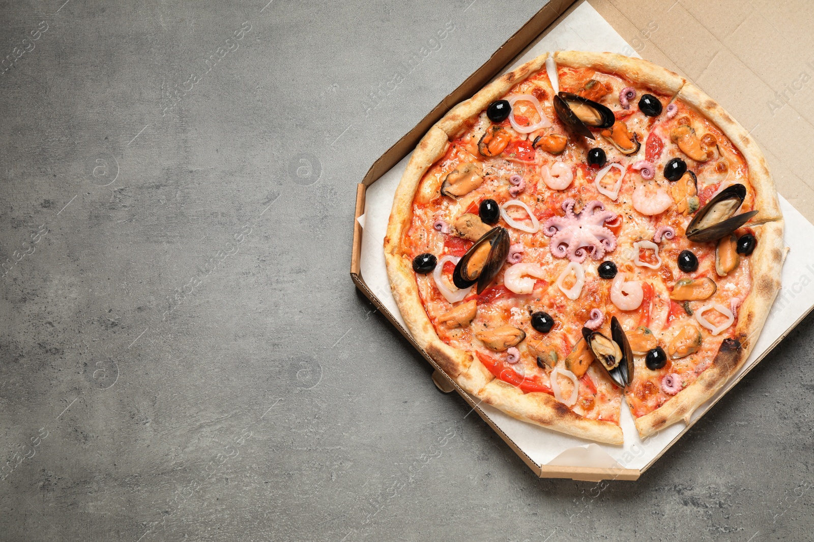 Photo of Delicious seafood pizza in box on grey table, top view. Space for text