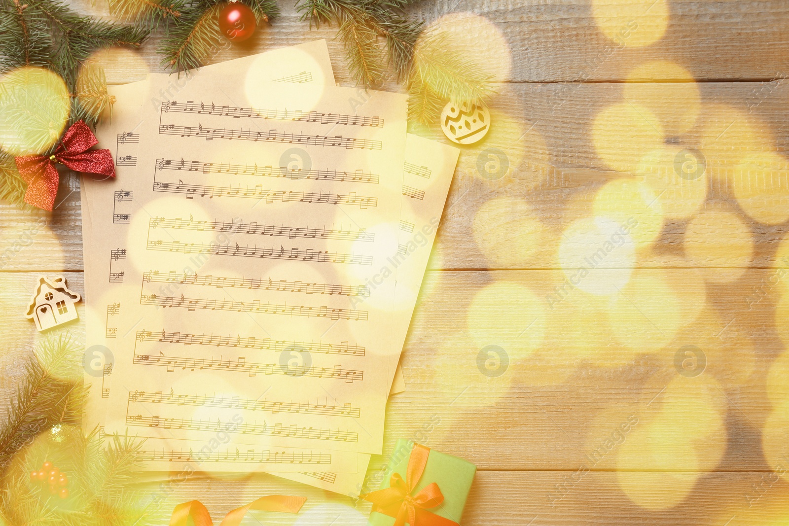 Image of Christmas and New Year music. Fir tree branch, festive decor and music sheets on wooden background, bokeh effect