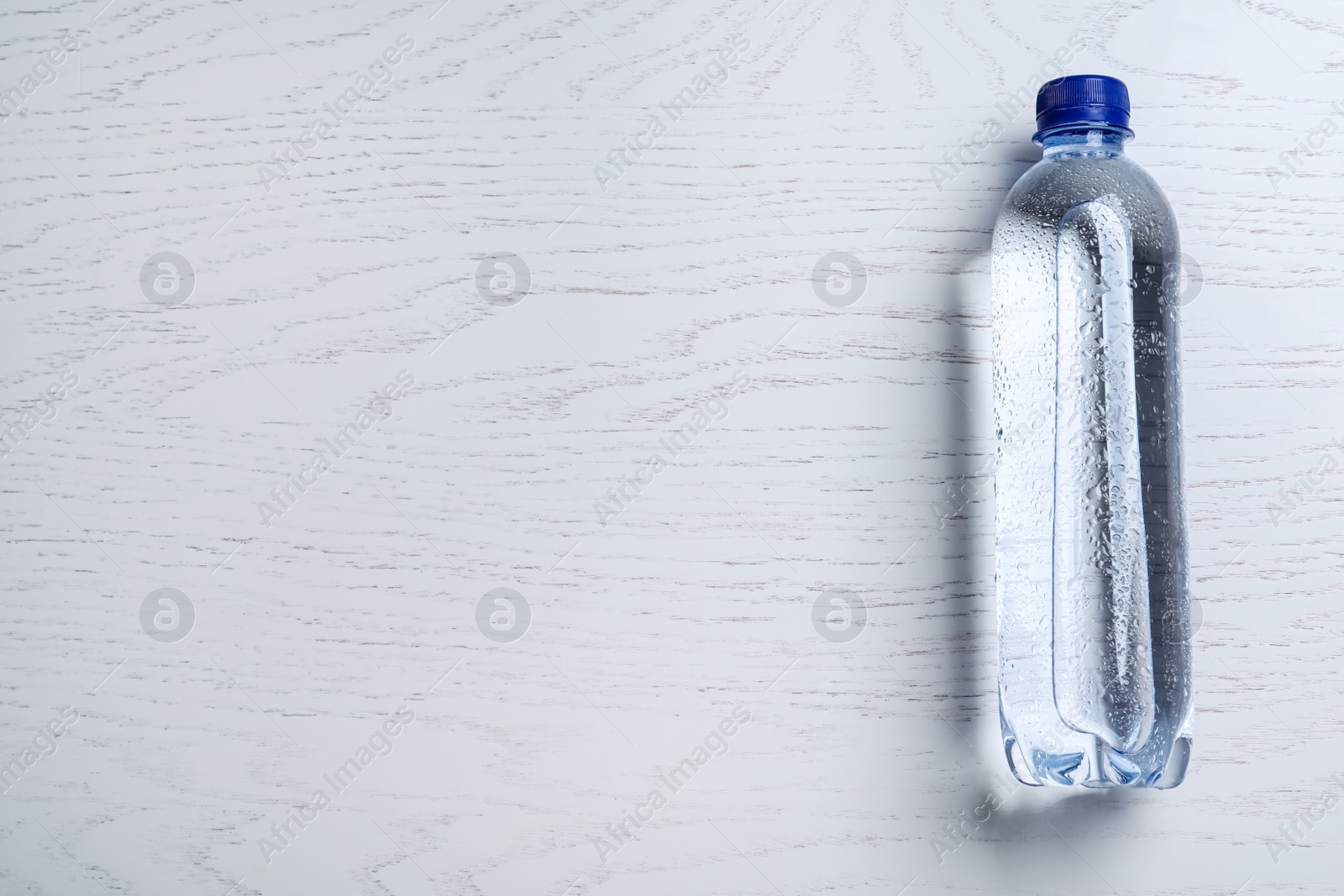 Photo of Plastic bottle with water on white wooden background, top view. Space for text