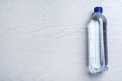 Photo of Plastic bottle with water on white wooden background, top view. Space for text