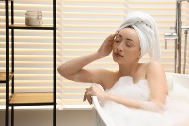 Beautiful woman taking bath with foam in tub indoors