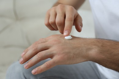 Photo of Man applying cream onto hand on sofa, closeup