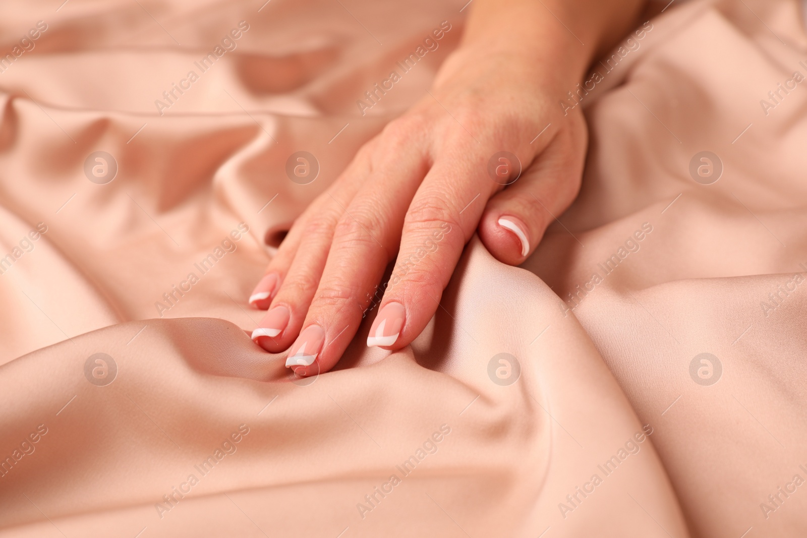 Photo of Woman touching smooth silky beige fabric, closeup
