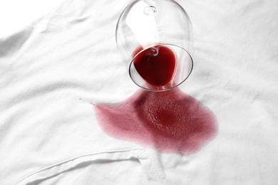 Photo of Overturned glass and spilled exquisite red wine on white t-shirt