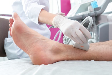 Photo of Doctor conducting ultrasound examination of patient's leg in clinic, closeup