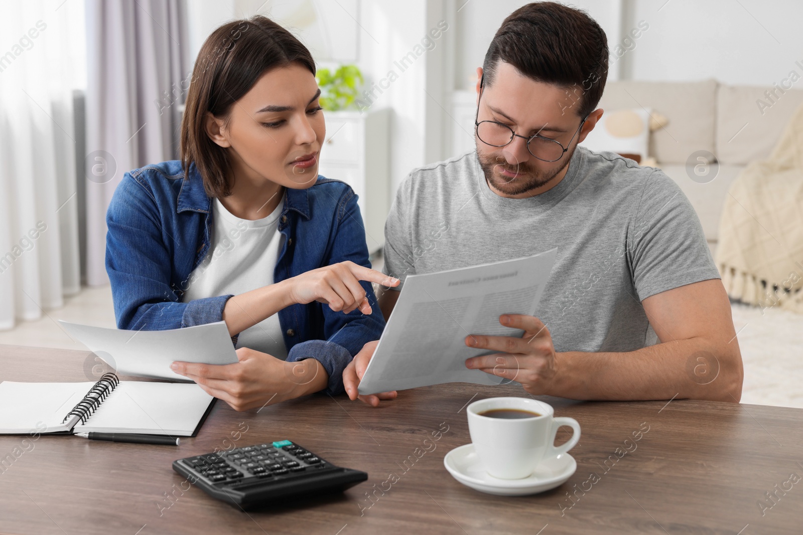 Photo of Young couple with papers discussing pension plan at wooden table indoors