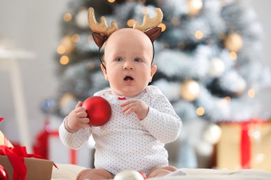 Photo of Little baby wearing funny deer antlers indoors. First Christmas