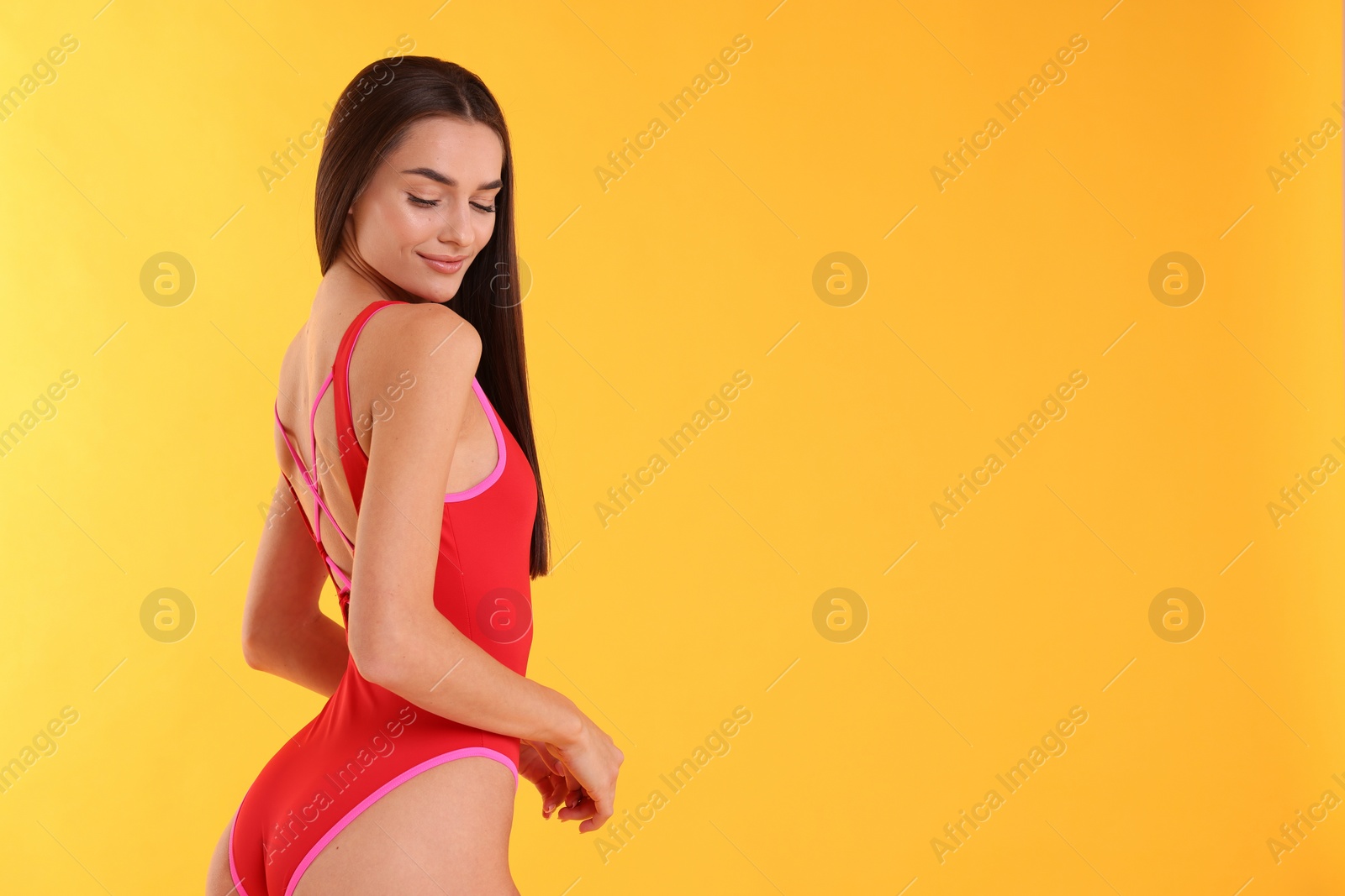 Photo of Young woman in stylish swimsuit on yellow background, space for text