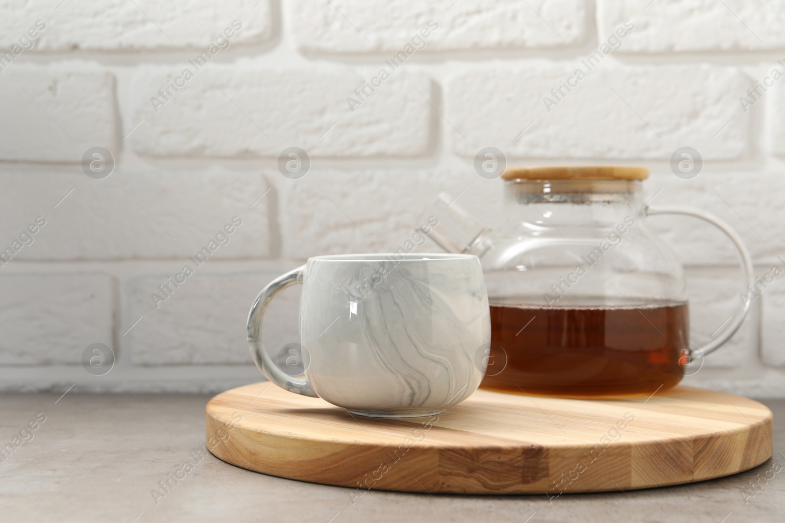 Photo of Aromatic tea in glass teapot and cup on gray table against white brick wall, space for text