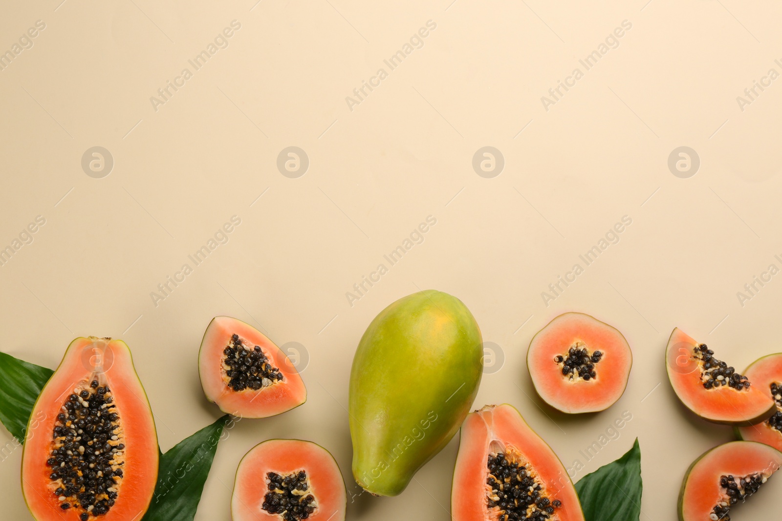 Photo of Fresh ripe papaya fruits with green leaves on beige background, flat lay. Space for text