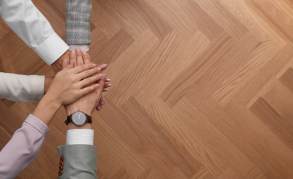 Photo of People holding hands together over wooden background, top view with space for text. Unity concept