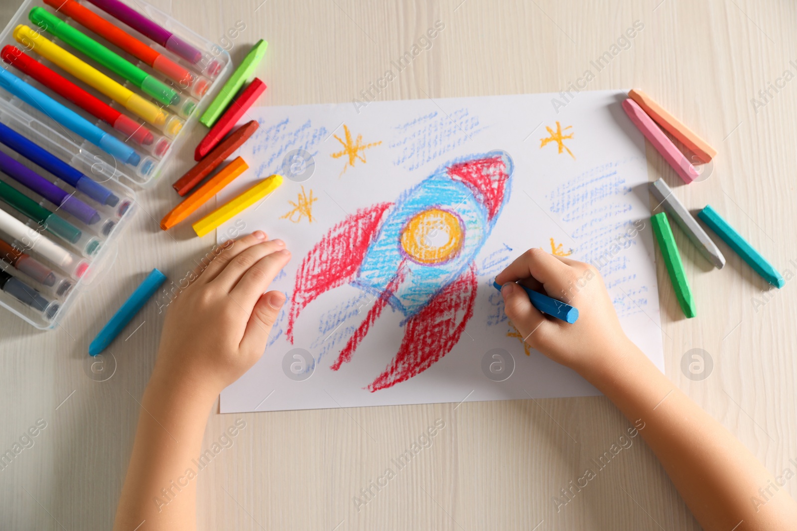 Photo of Little boy drawing rocket with soft pastel at wooden table, top view. Child`s art
