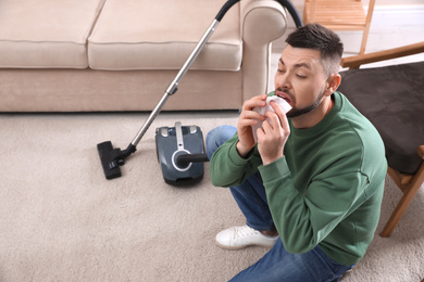 Man with vacuum cleaner suffering from dust allergy at home