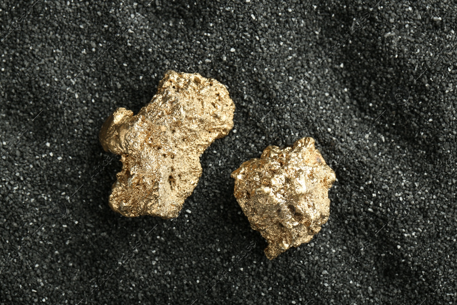 Photo of Shiny gold nuggets on black sand, top view