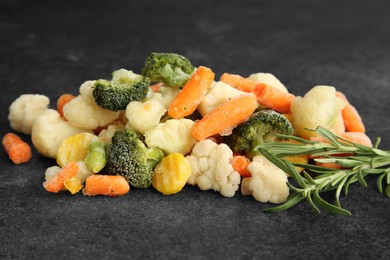 Photo of Mix of different frozen vegetables and rosemary on gray table, closeup