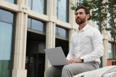 Photo of Handsome businessman with laptop on city street