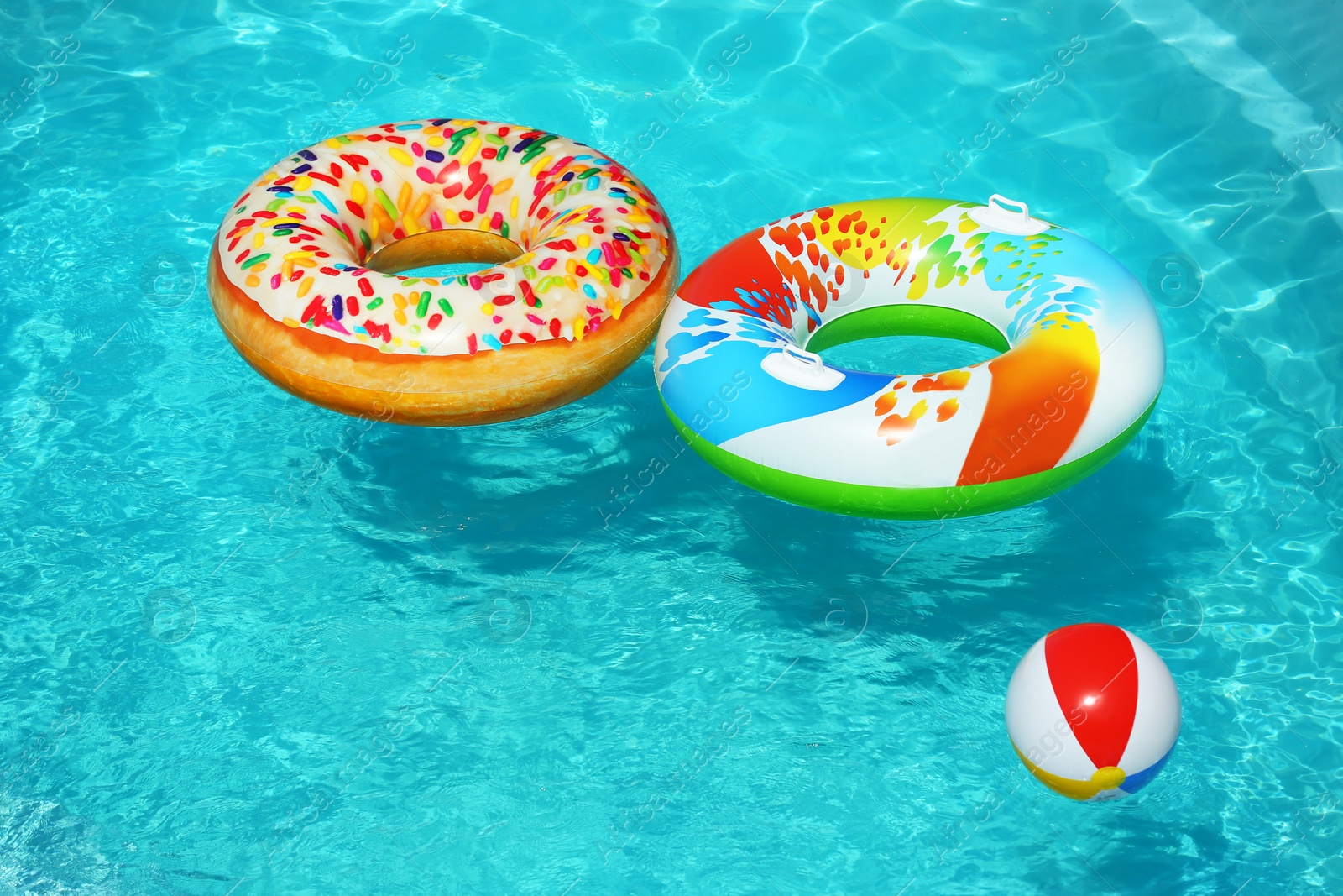 Photo of Bright inflatable rings and beach ball floating in swimming pool on sunny day. Space for text