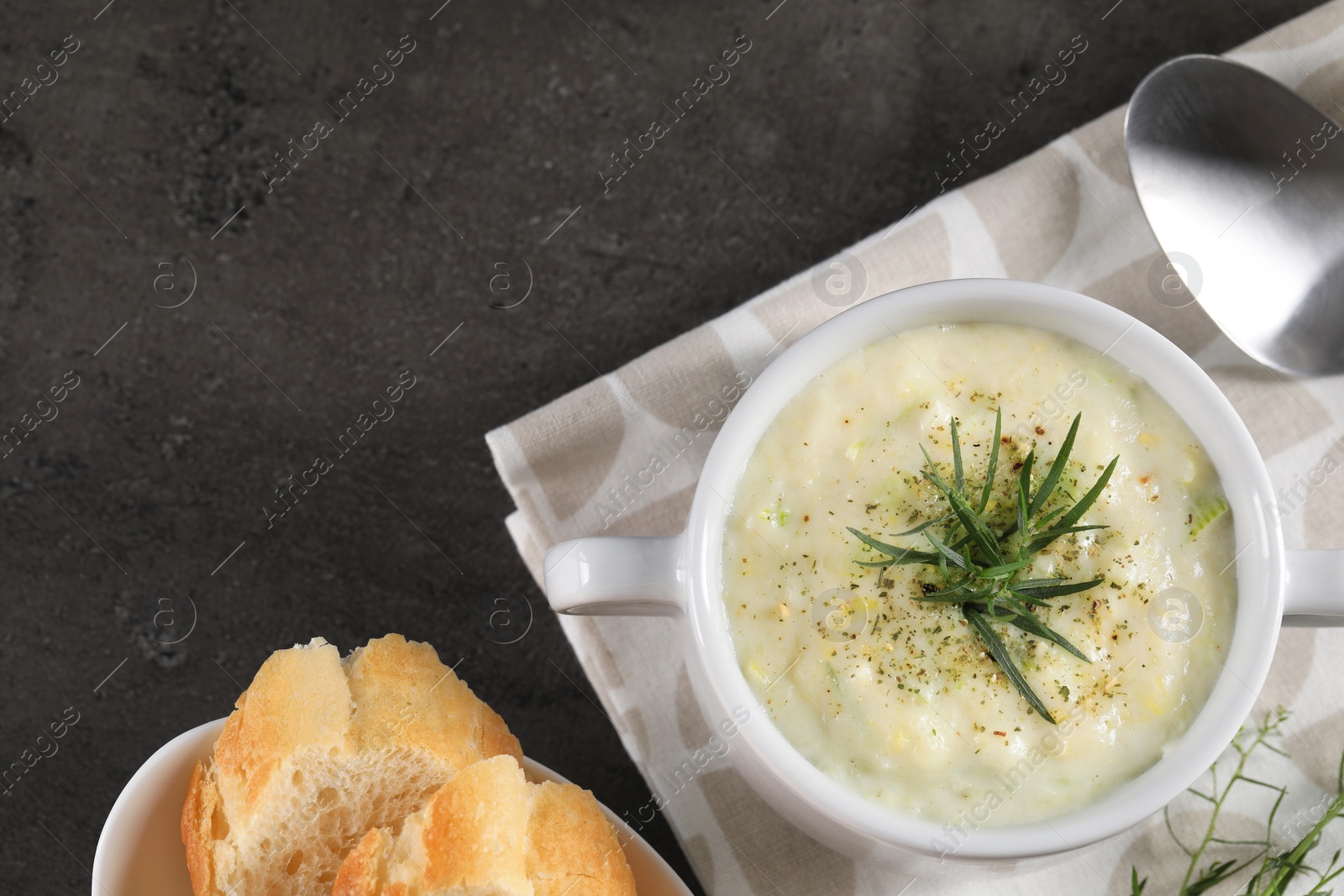 Photo of Delicious cream soup with tarragon, spices and potato in bowl served on dark textured table, flat lay. Space for text