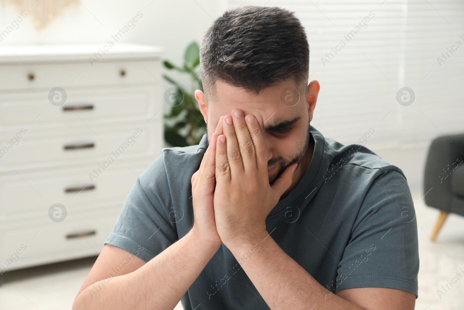 Photo of Sad man covering face with hands at home