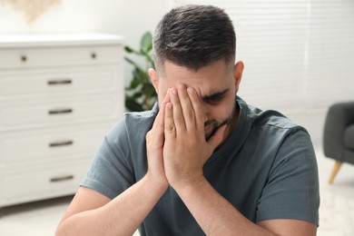 Sad man covering face with hands at home