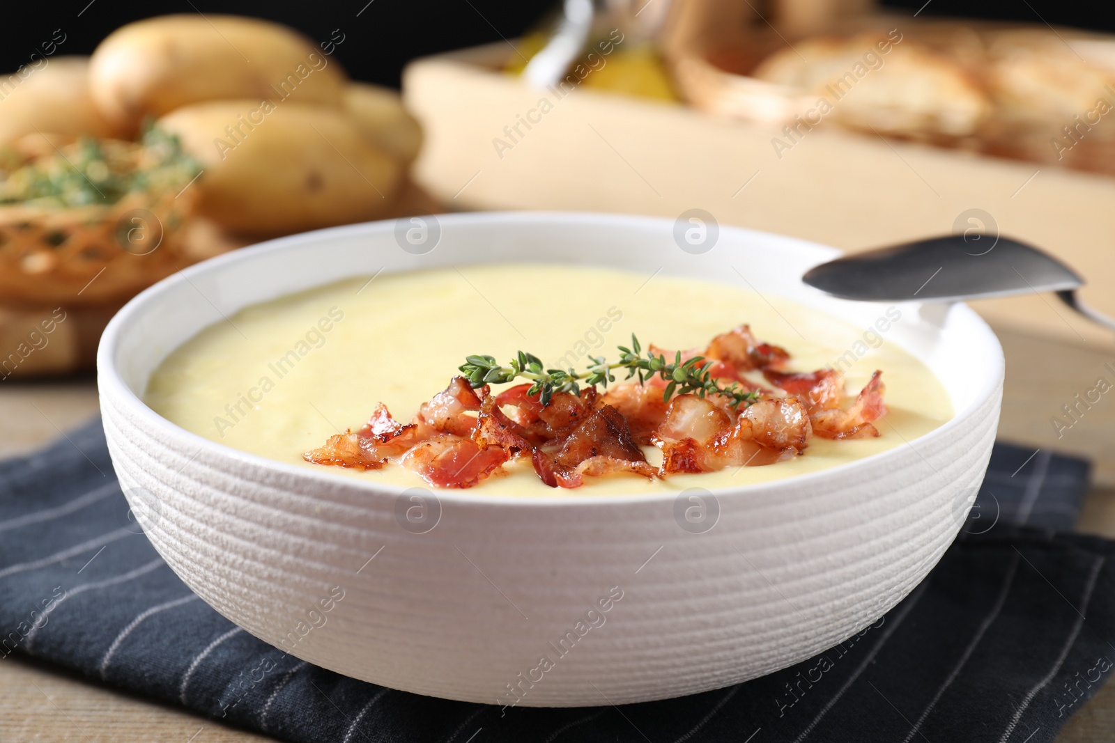 Photo of Tasty potato soup with bacon in bowl and spoon on table, closeup