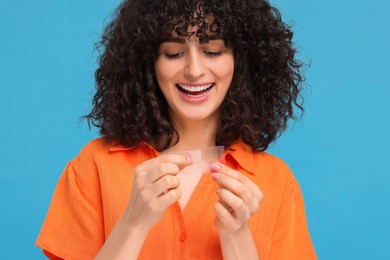 Young woman holding teeth whitening strips on light blue background