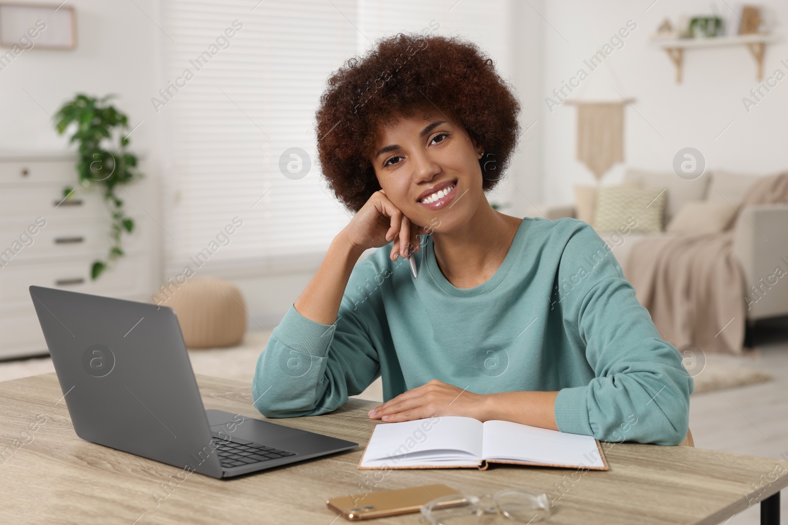 Photo of Young woman using laptop at wooden desk in room