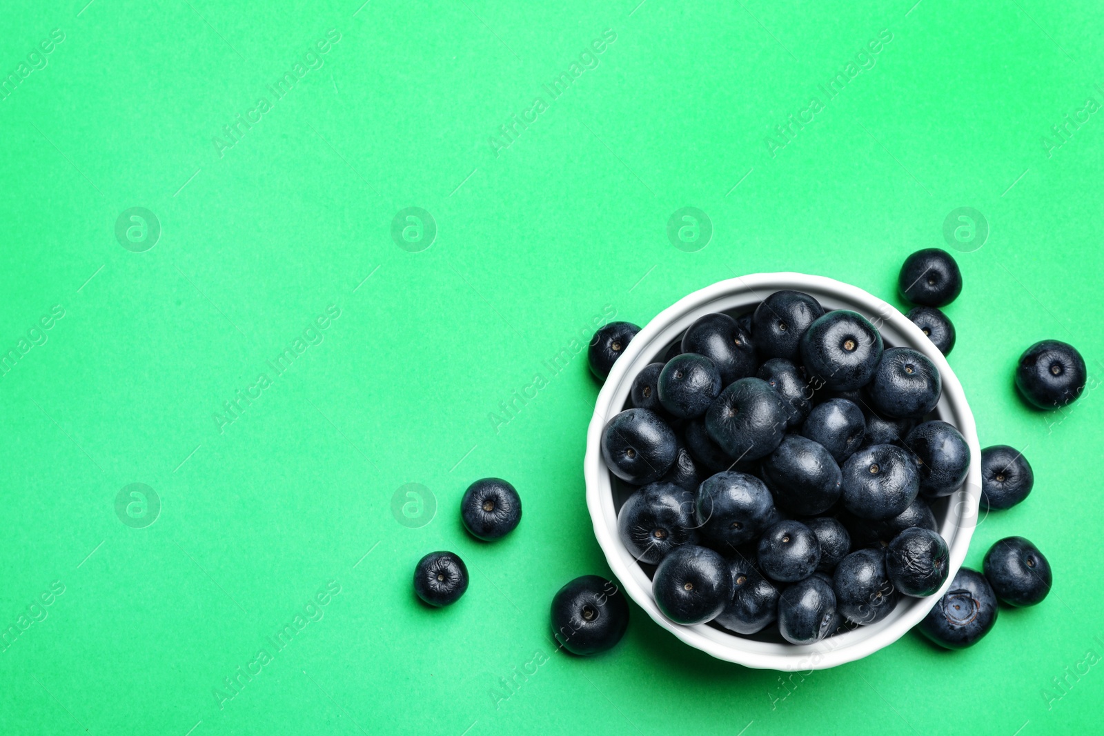 Photo of Bowl of fresh acai berries on green background, flat lay. Space for text