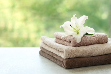 Stack of clean towels with lily on table against blurred background. Space for text