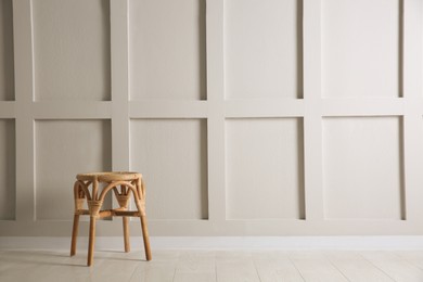 Photo of Stylish wooden stool near white wall, space for text. Interior element