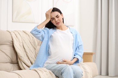 Photo of Pregnant woman suffering from headache on sofa at home