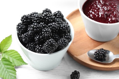 Photo of Fresh ripe blackberries, tasty jam and leaves on white wooden table, closeup