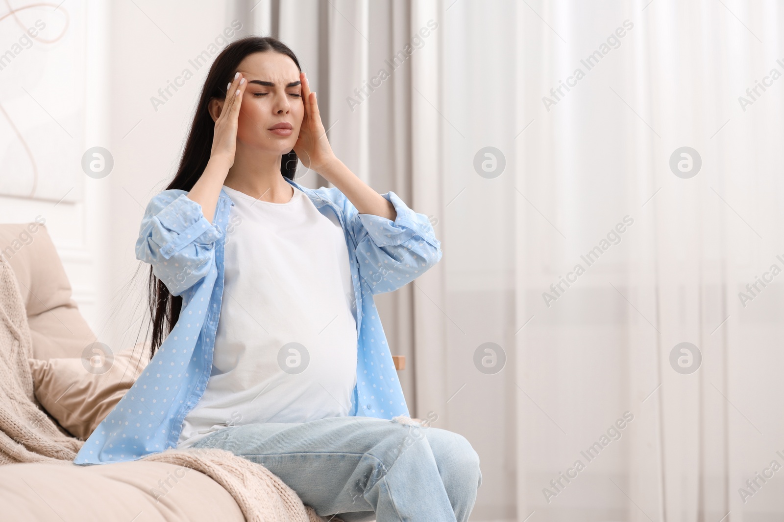 Photo of Pregnant woman suffering from headache on sofa at home, space for text