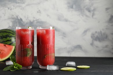 Glasses of delicious fresh watermelon juice, lime, mint and ice on black wooden table against textured wall. Space for text