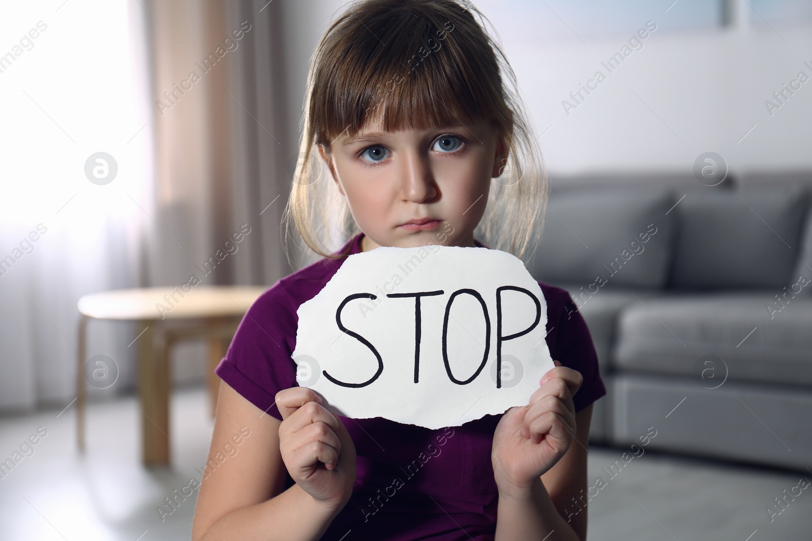 Photo of Abused little girl with sign STOP indoors. Domestic violence concept