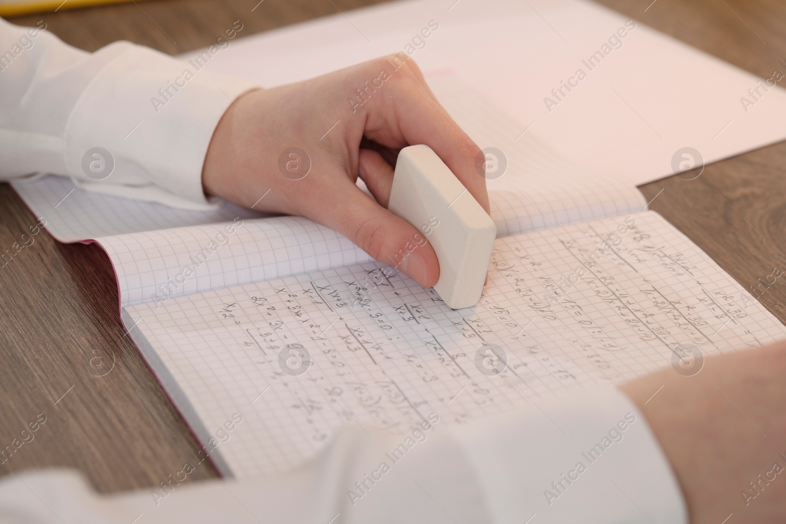 Photo of Girl erasing mistake in her notebook at wooden desk, closeup