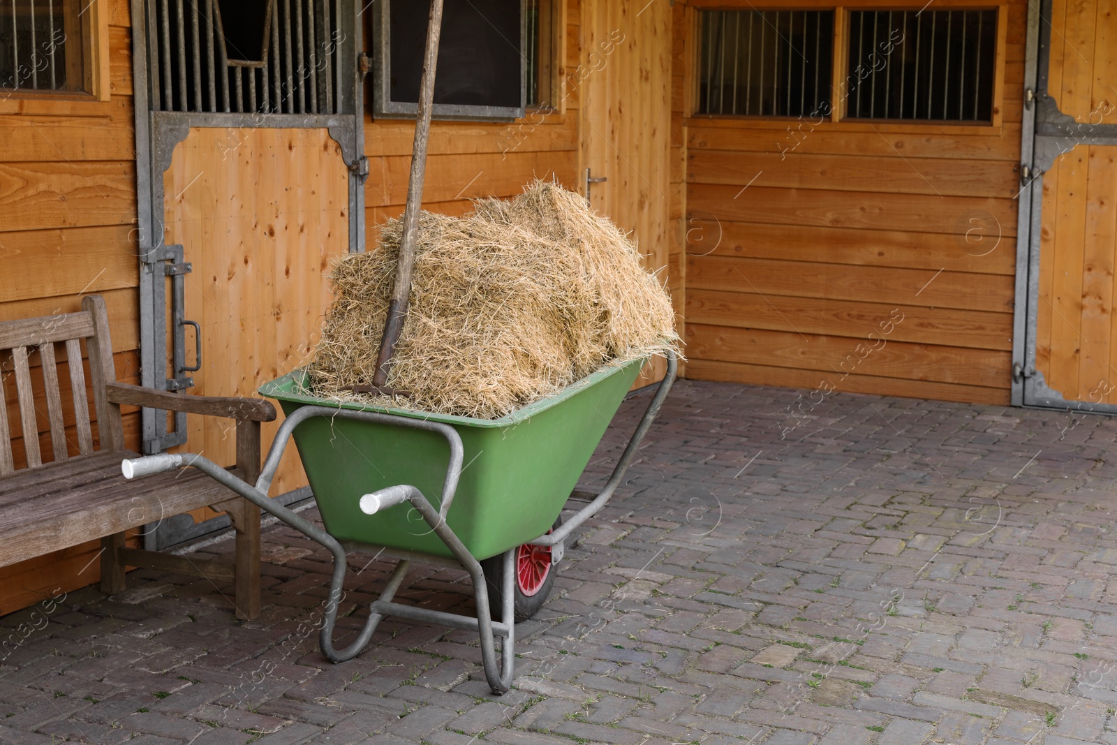 Photo of Wheelbarrow with hay near wooden stable outdoors