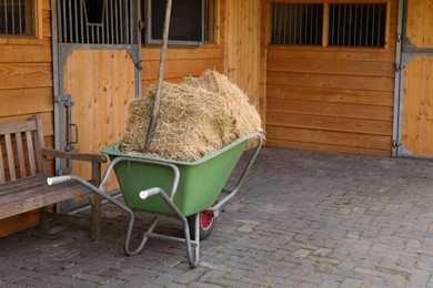 Wheelbarrow with hay near wooden stable outdoors