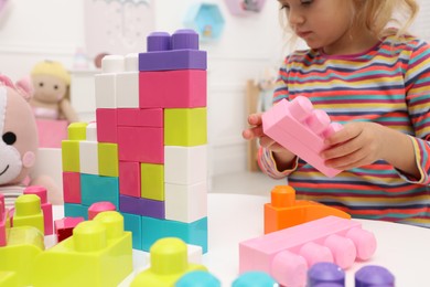 Cute little girl playing with colorful building blocks at table indoors, closeup