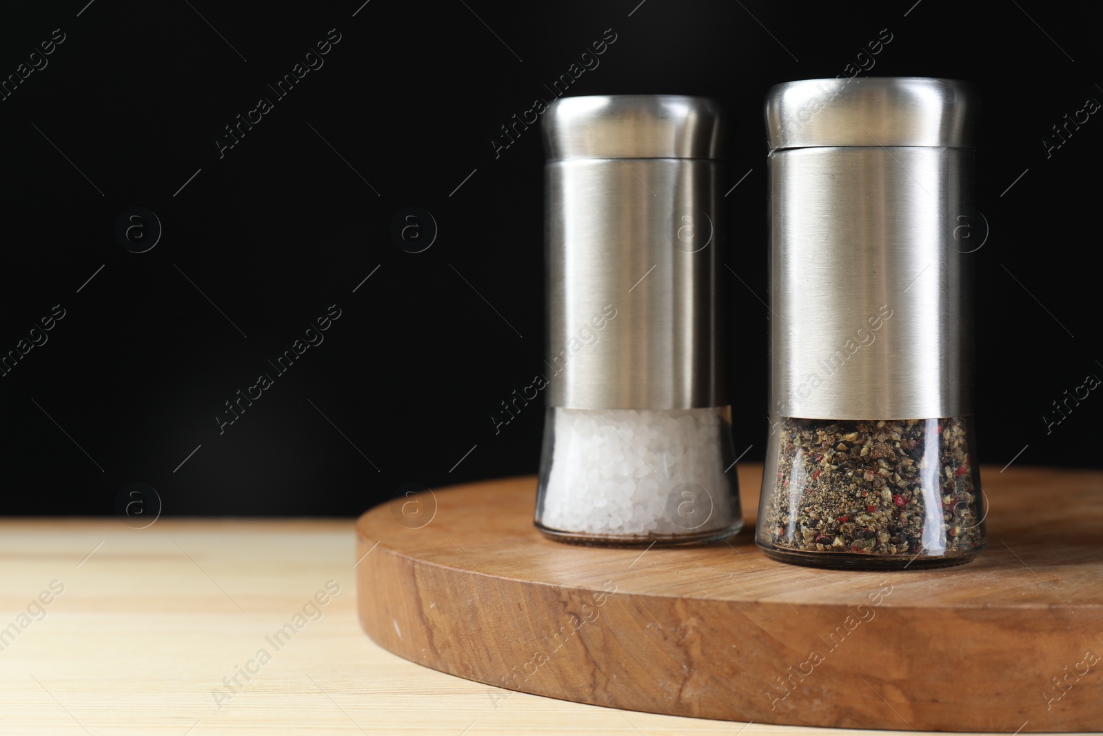 Photo of Salt and pepper shakers on wooden table against black background, space for text