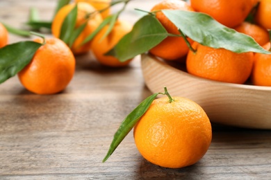 Photo of Fresh ripe tangerines with green leaves on wooden table