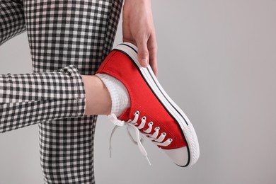 Photo of Woman putting on red classic old school sneaker against light grey background, closeup. Space for text