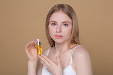 Photo of Beautiful young woman with bottle of essential oil on brown background