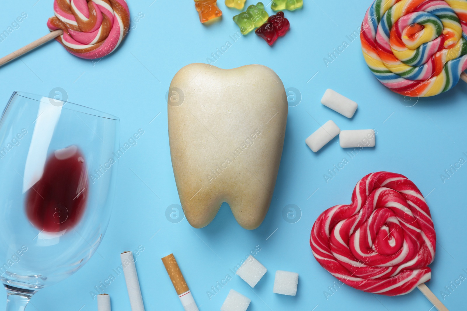 Photo of Tooth model, unhealthy food and cigarettes on light blue background, flat lay