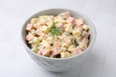 Photo of Tasty Olivier salad with boiled sausage in bowl on white tiled table, closeup