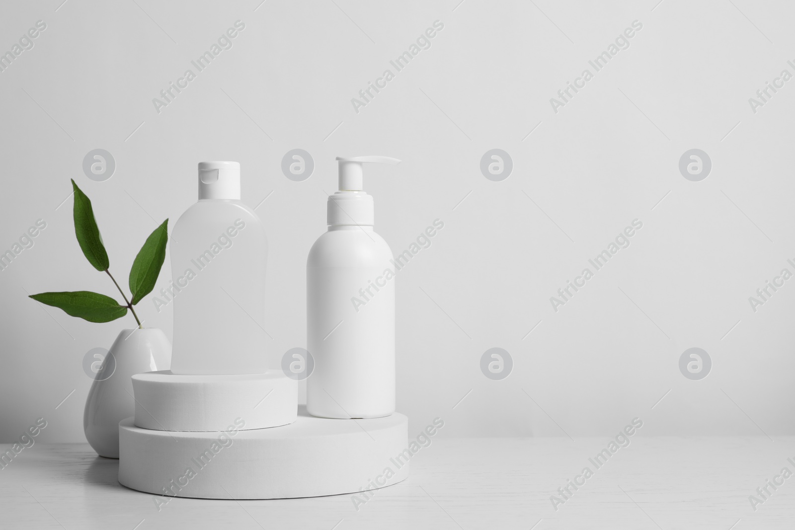 Photo of Bottles of cosmetic products and leaves on white wooden table. Space for text