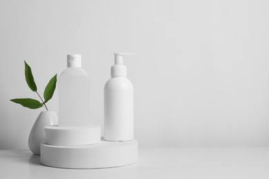 Bottles of cosmetic products and leaves on white wooden table. Space for text